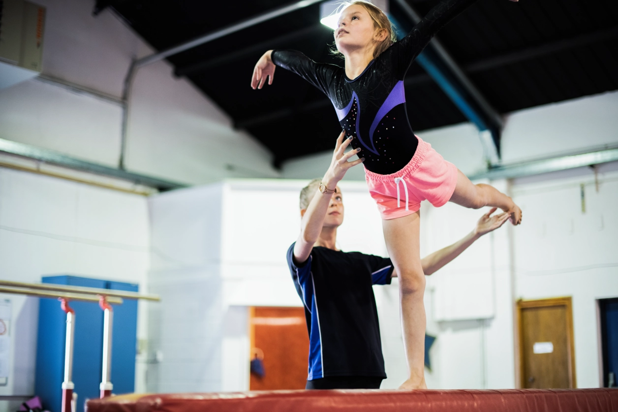 Coach assisting gymnast on balance beam.